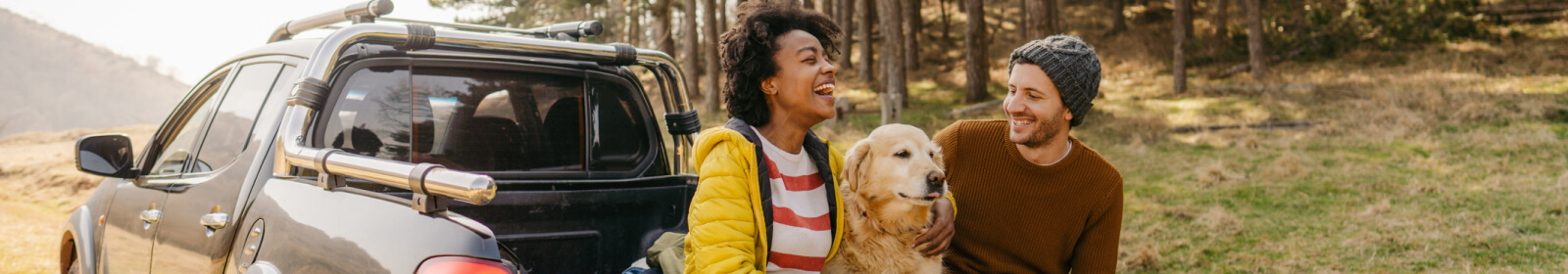 a couple sitting on a truck bed with their dog